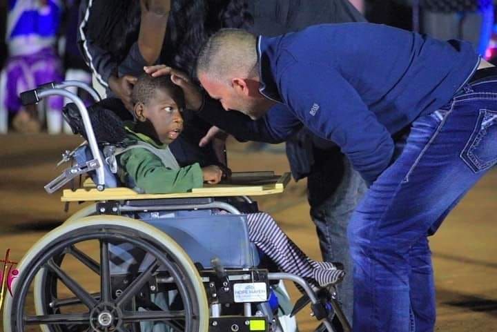 A person in a wheelchair is being comforted by another person. Outdoor setting, night.