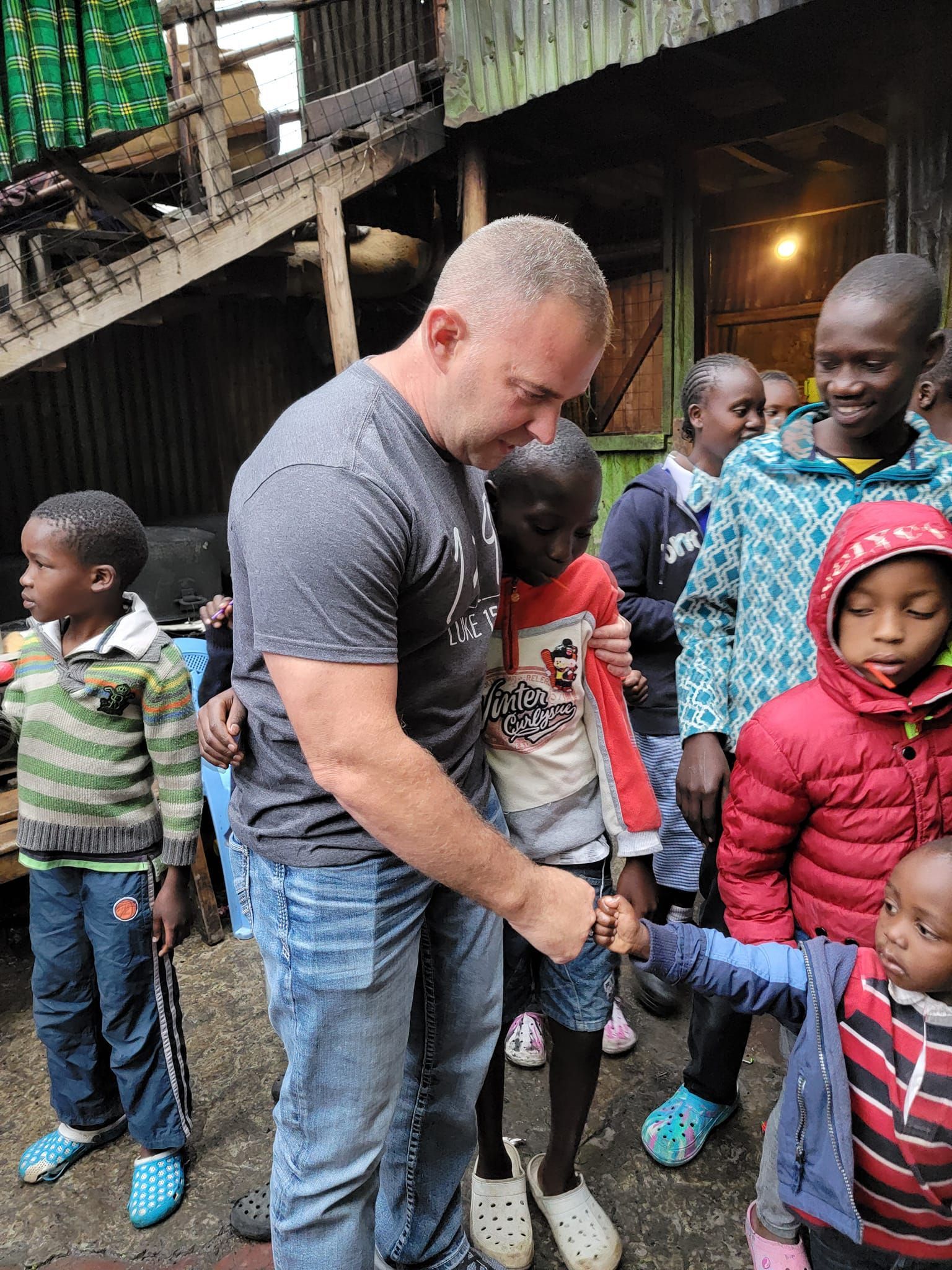 Man holding a child's hand surrounded by children outside a building.