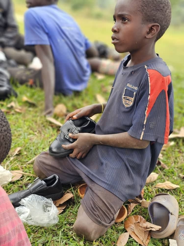 Boy with amputated legs sits on grass, holding a shoe. Others sit nearby.