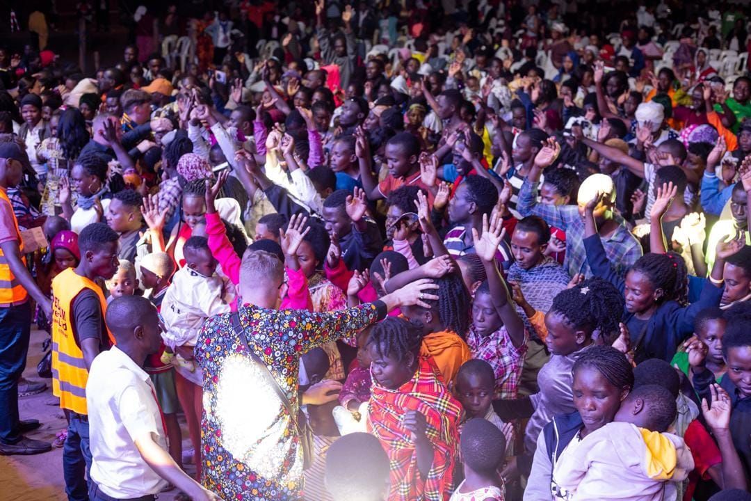 Large crowd of people, arms raised, appear to be at a concert or event.