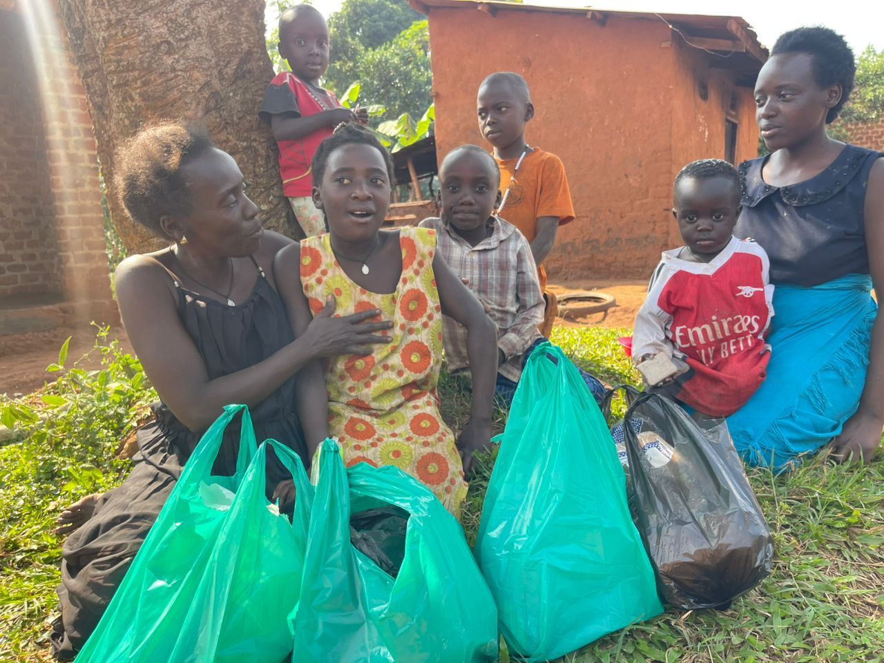 People gathered outdoors, receiving green bags. Children and a woman in a floral dress show emotion.