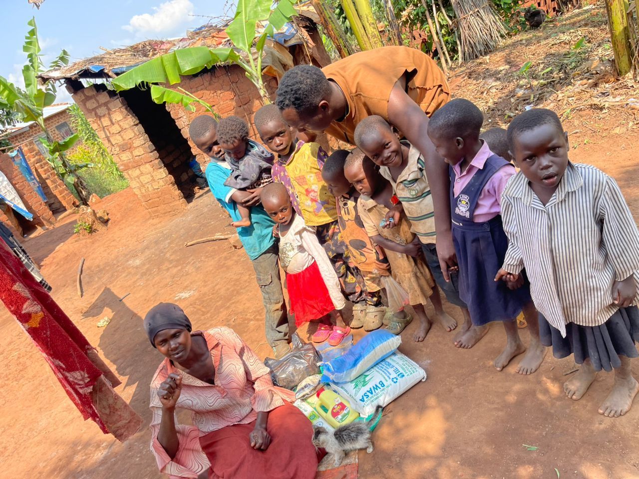 Group of children and adults next to food supplies in front of a brick building.