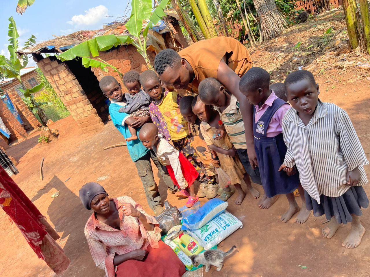 Group of children and a man with an older woman, near a building. They are gathered around a few bags.