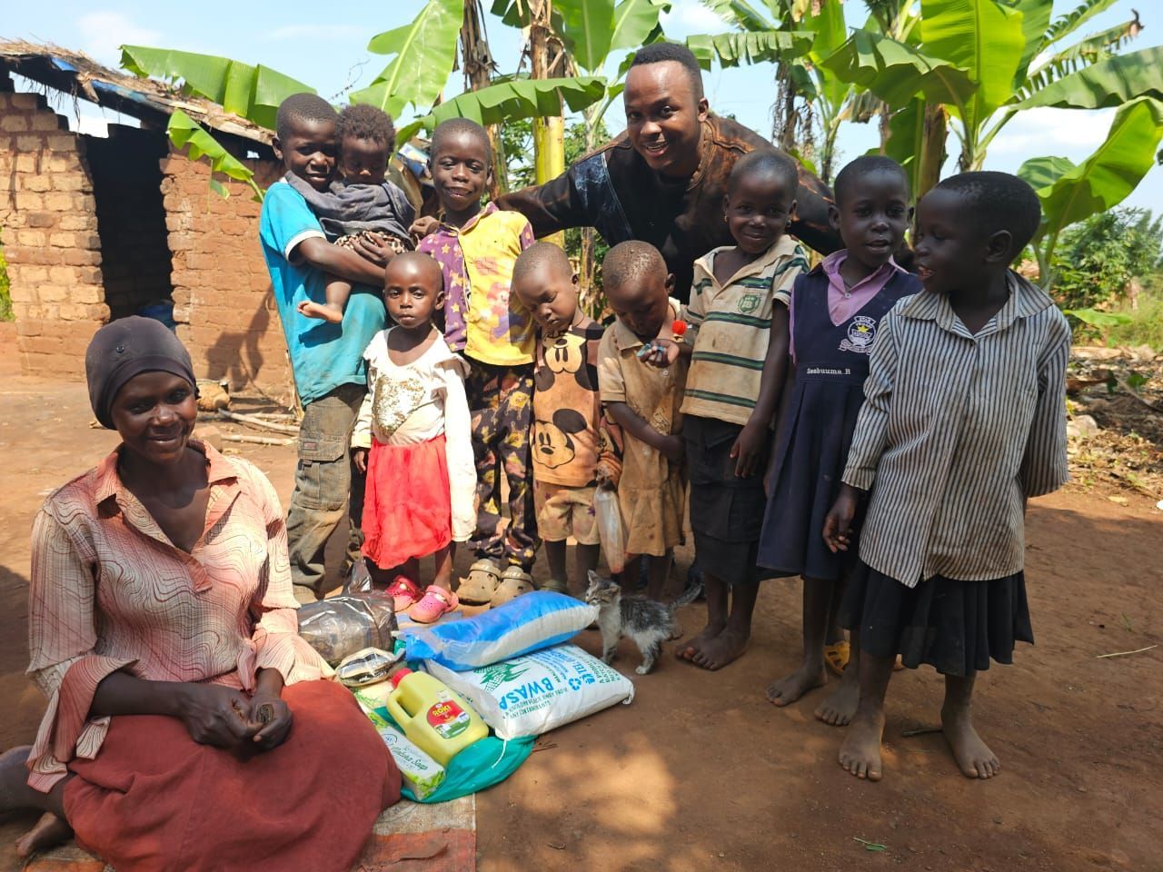 A group of children and two adults pose outdoors with bags of food.
