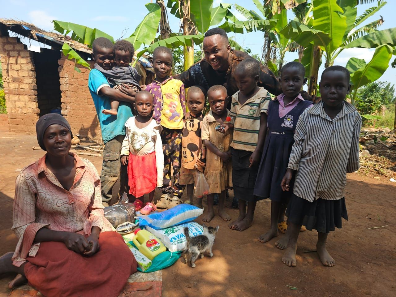 A group of children and adults pose with food donations outside a simple home.