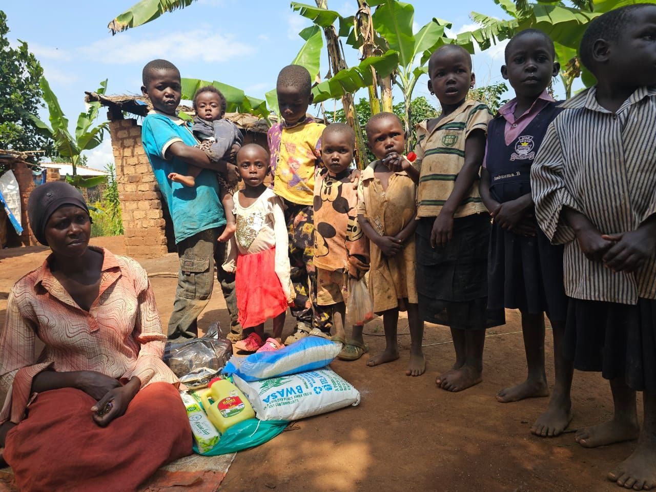 Woman sits with children and bags of supplies outside a building.