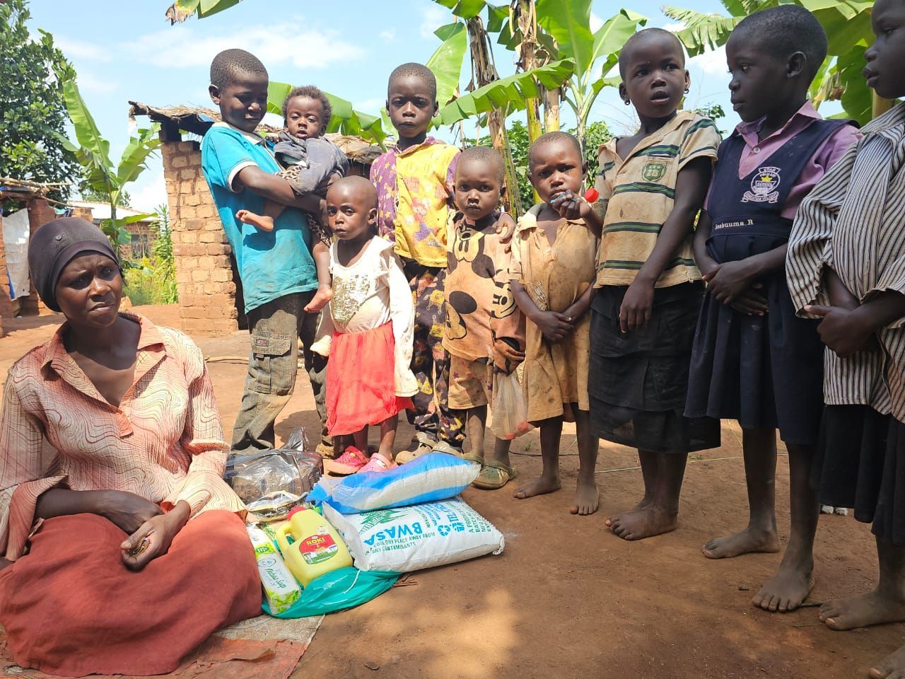 Woman seated with children; food items in front. Outdoors, sunny.