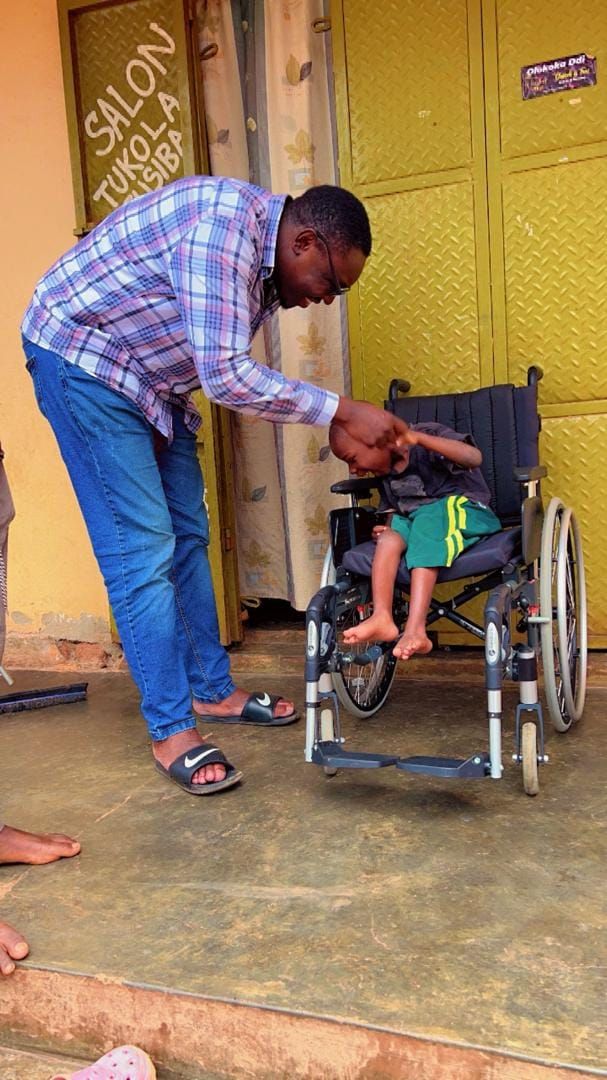 Man assisting a person in a wheelchair; outdoors by a building with a yellow door.