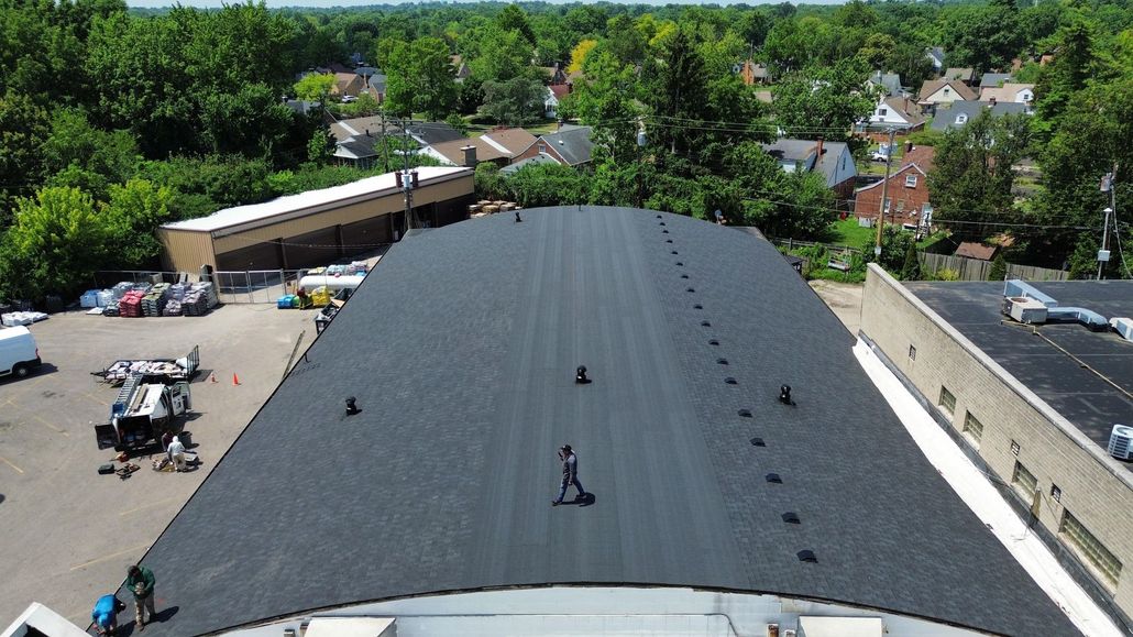 Overhead view of a black, flat roof with a person walking. Buildings and trees are in the background.