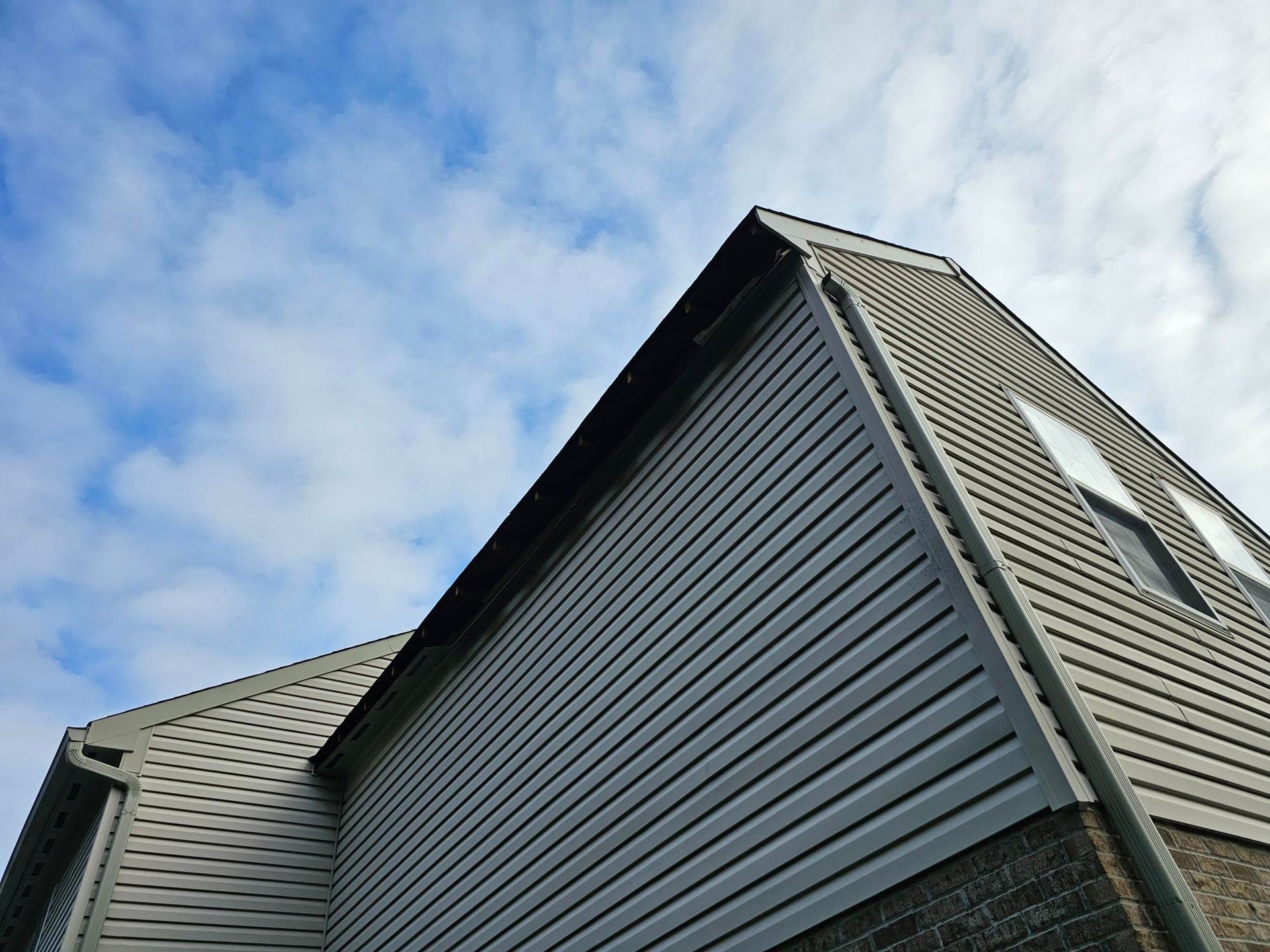 Low-angle shot of a two-story house with gray siding against a partly cloudy blue sky.