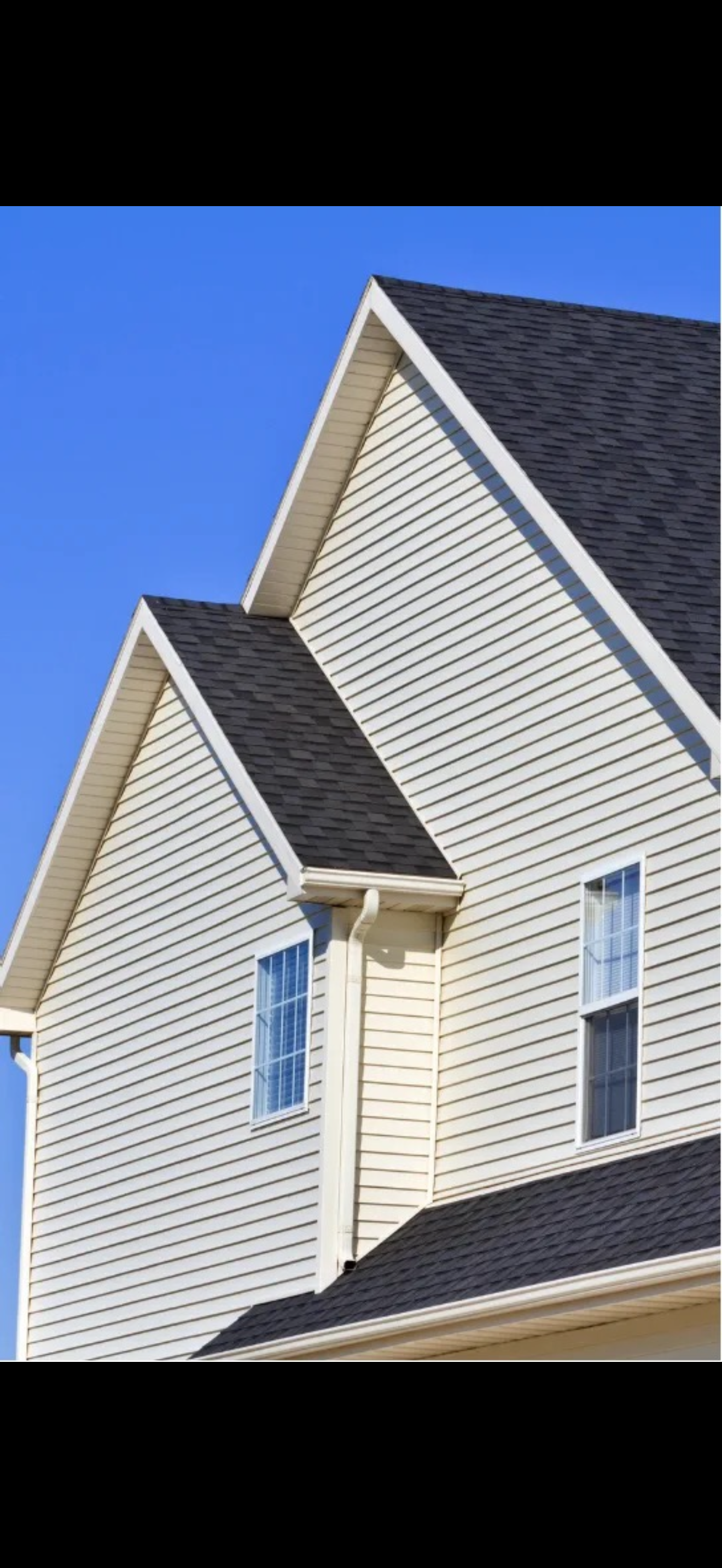 Side view of a house with white siding, black roof, and two windows against a bright blue sky.
