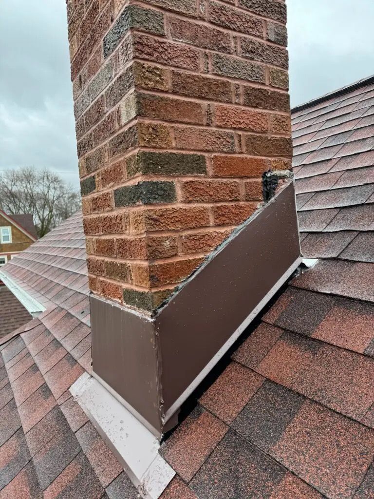 Brick chimney with brown metal flashing on a shingled roof.