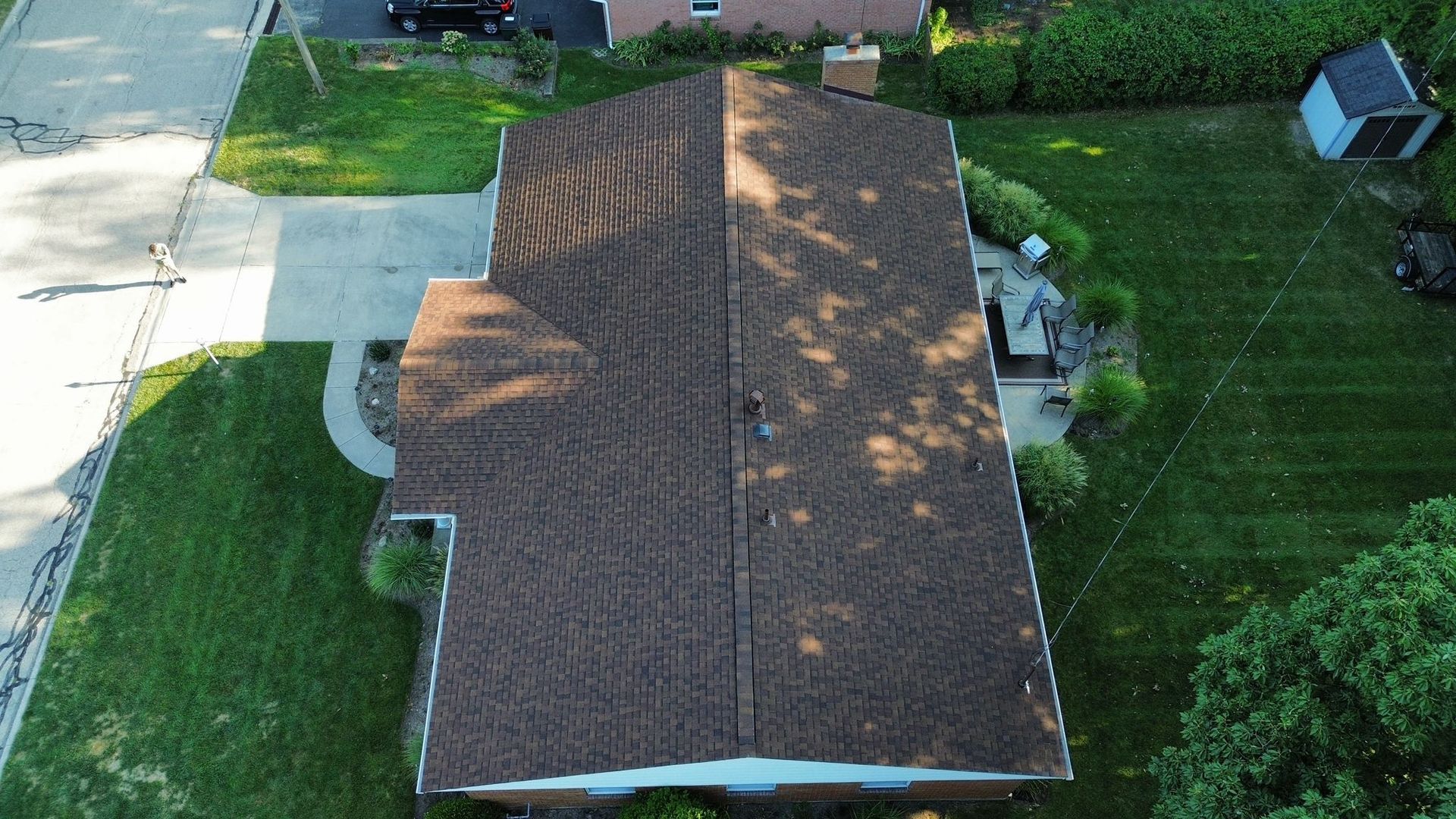 Overhead view of a house with a brown shingled roof, driveway, and surrounding green lawn.