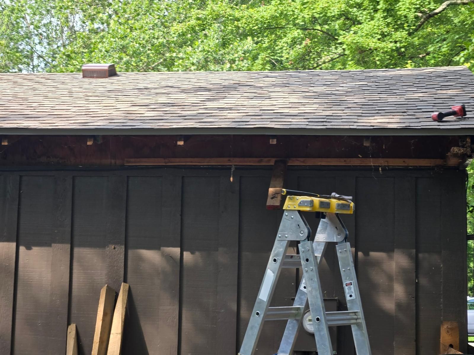 A person working on the edge of a brown roof, using a ladder and tools.