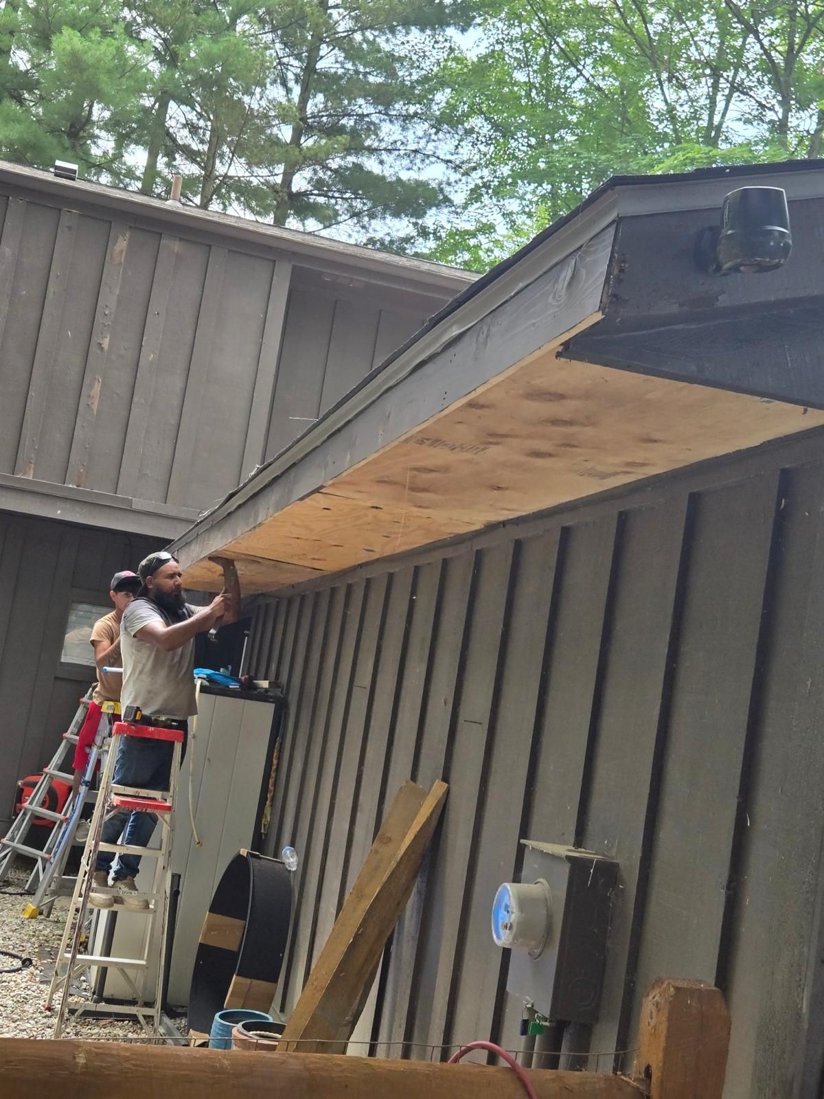 Two people installing wooden paneling on the exterior of a brown building.