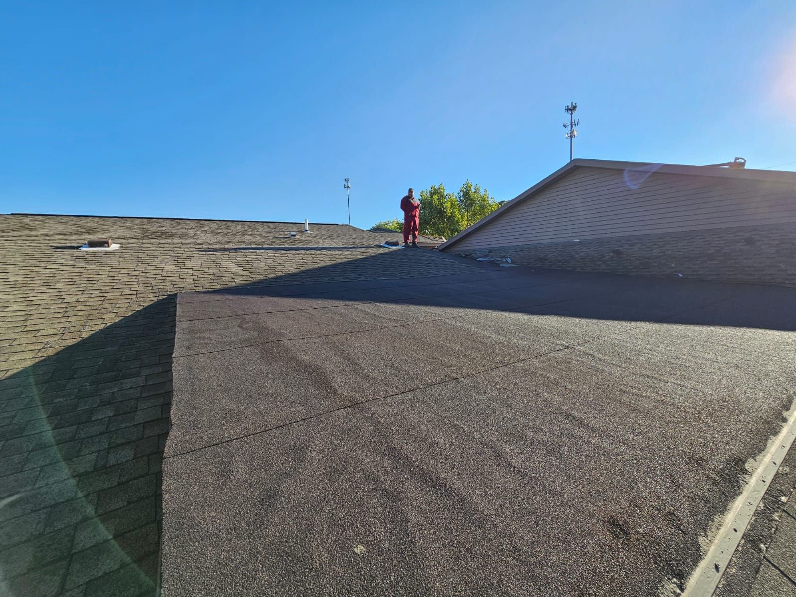 Person in red jumpsuit on a shingled roof under a clear blue sky.