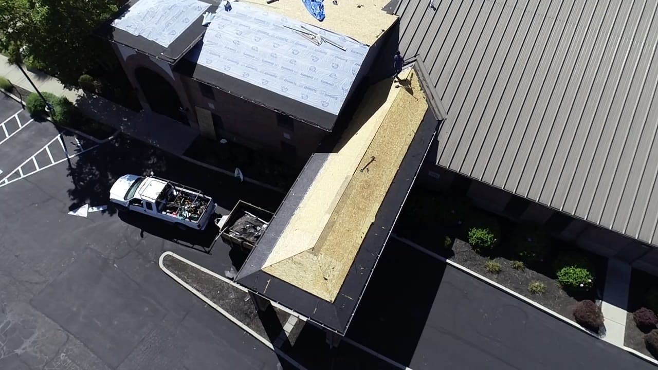 Overhead view of a building with roof being repaired. A white truck and dumpster are nearby.