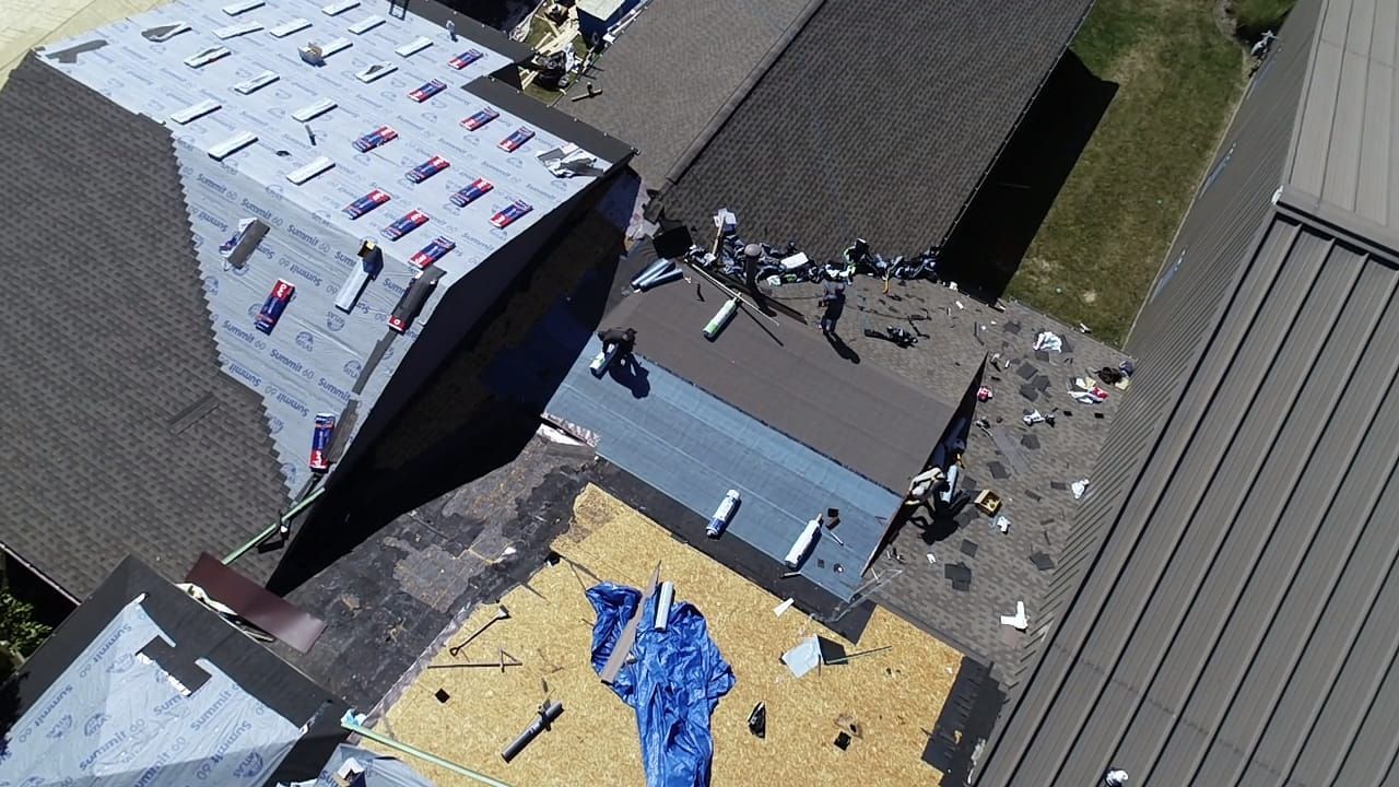 Aerial view of multiple roofs; some with shingles, some under repair, and others covered with debris.