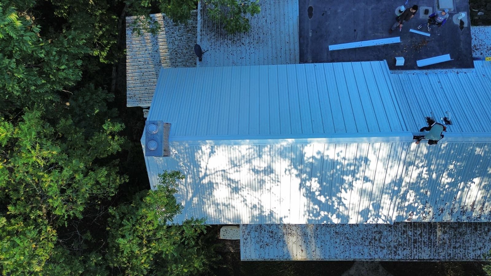 Overhead view of a building with a newly installed silver metal roof; two people on roof.