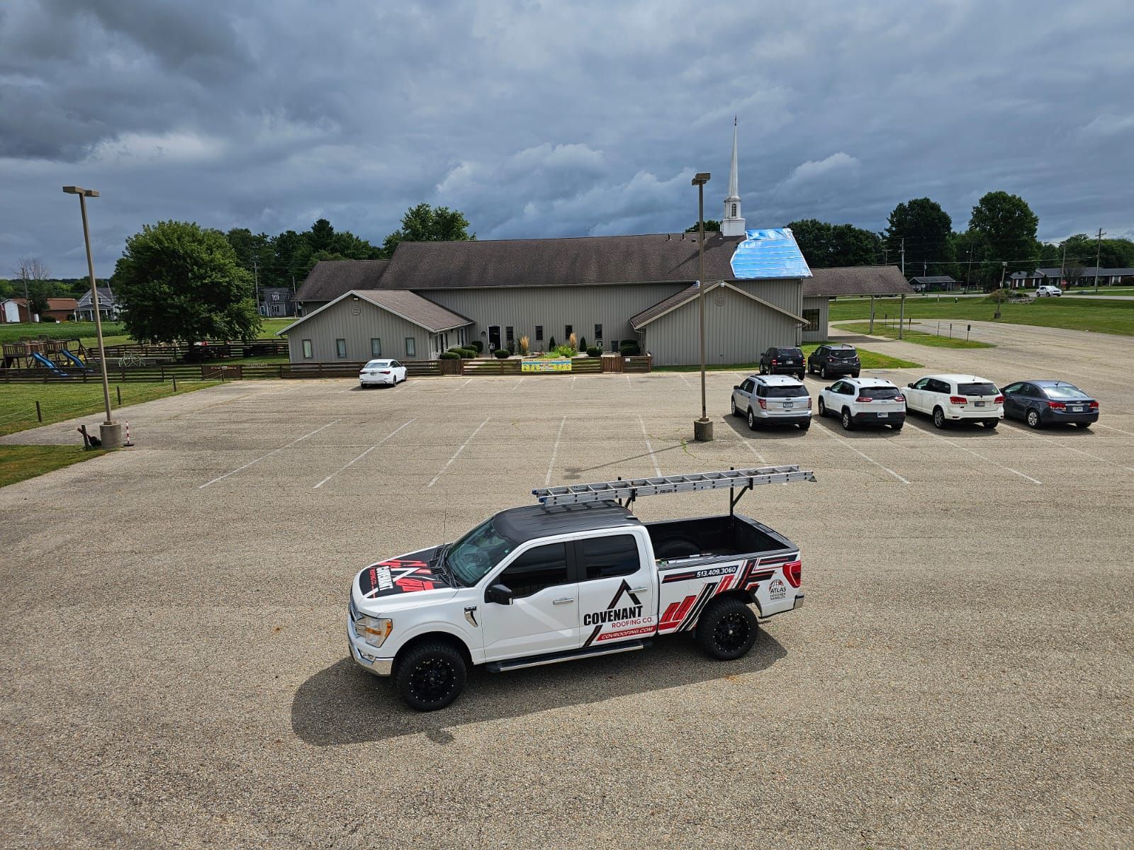 White truck with ladder parked in church parking lot; church in background. Overcast sky.