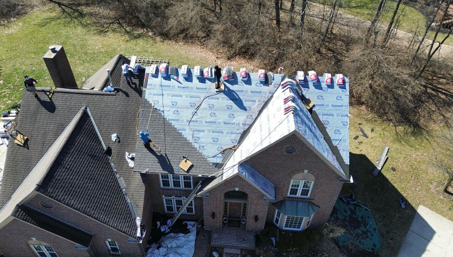 Roofers installing shingles on a two-story brick home, viewed from above.