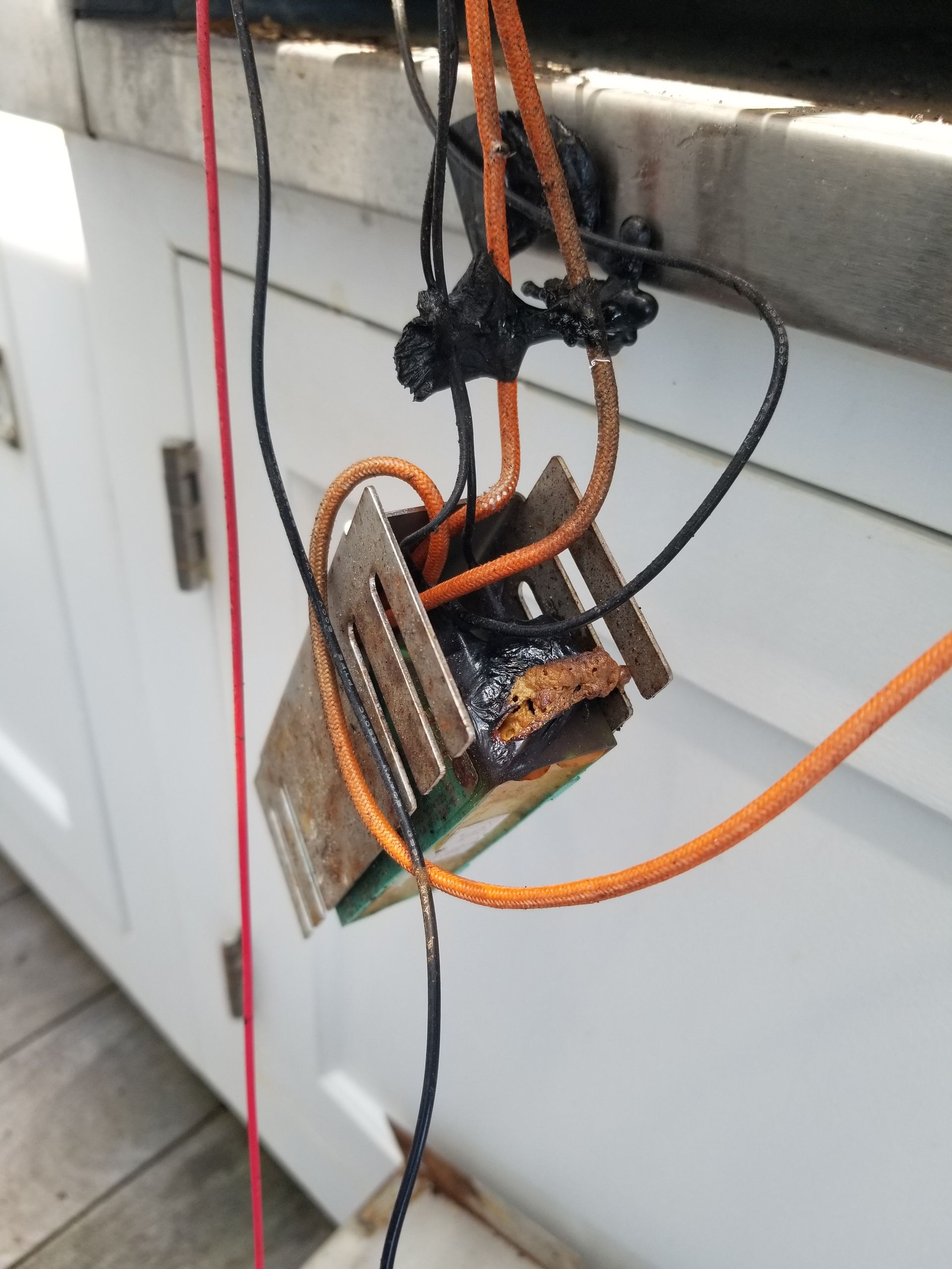 Damaged electrical component with melted black material and wires; orange and black wires hang down.