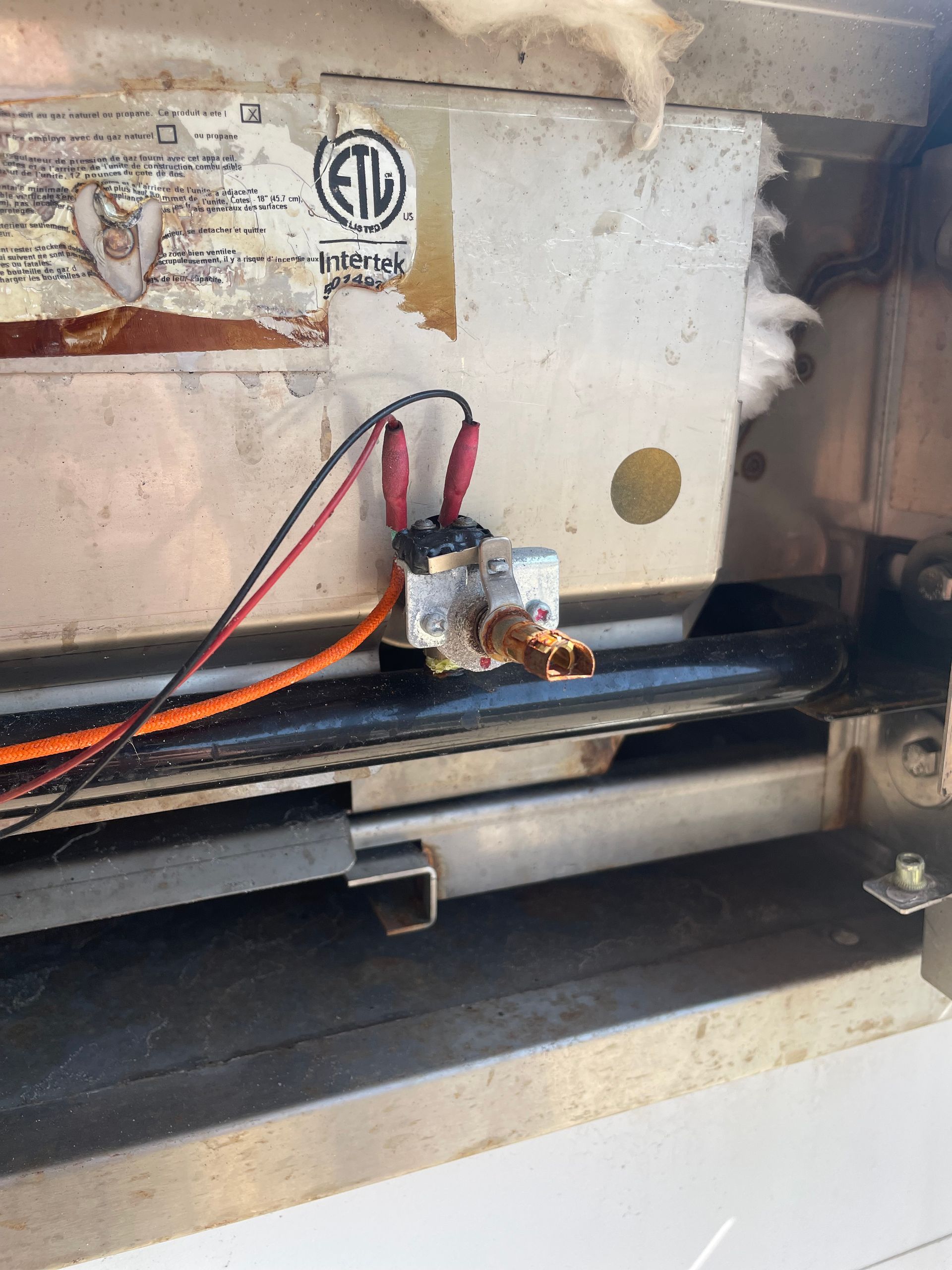 Close-up of a metal appliance component with electrical wiring and a rusty fitting.