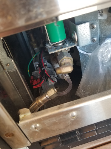 Inside an appliance, a gas valve is connected to a flexible hose and electrical wiring.