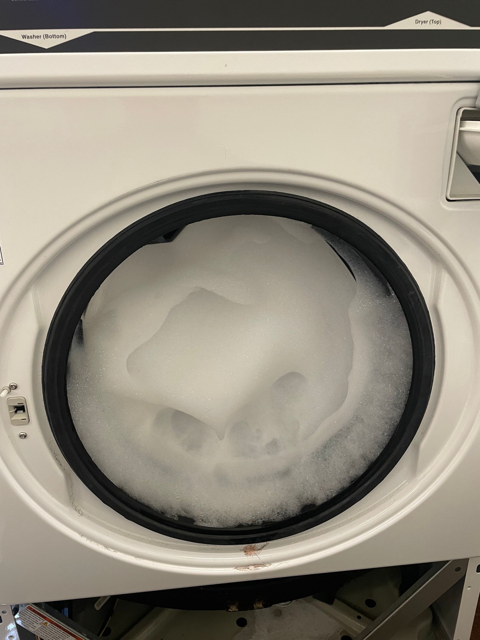 Washing machine door open, filled with excessive white foam, possibly due to too much soap.