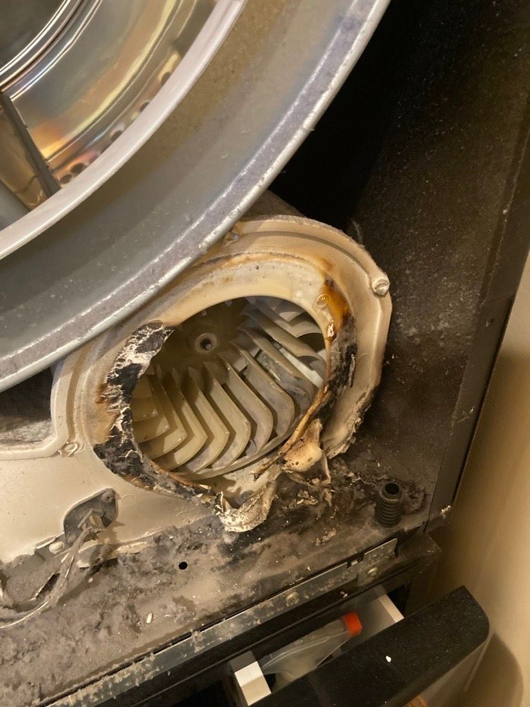Damaged dryer blower wheel and housing; interior view with metal drum at top, black frame.