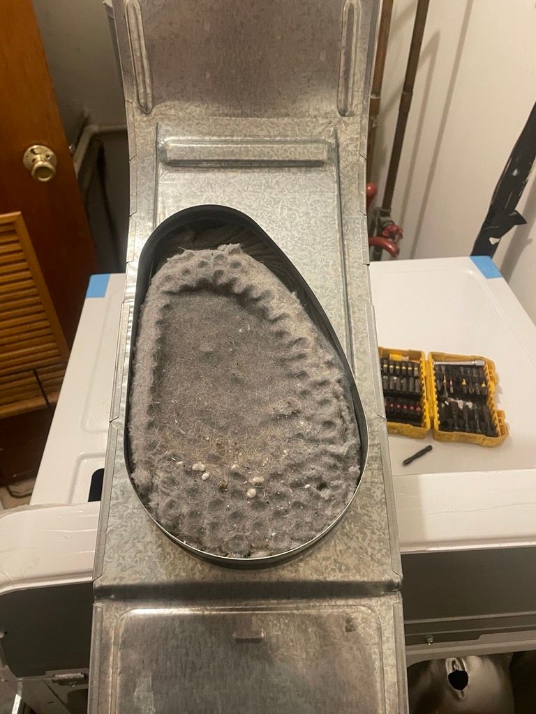 A dryer vent with a thick layer of lint inside. A small screwdriver set is to the right.