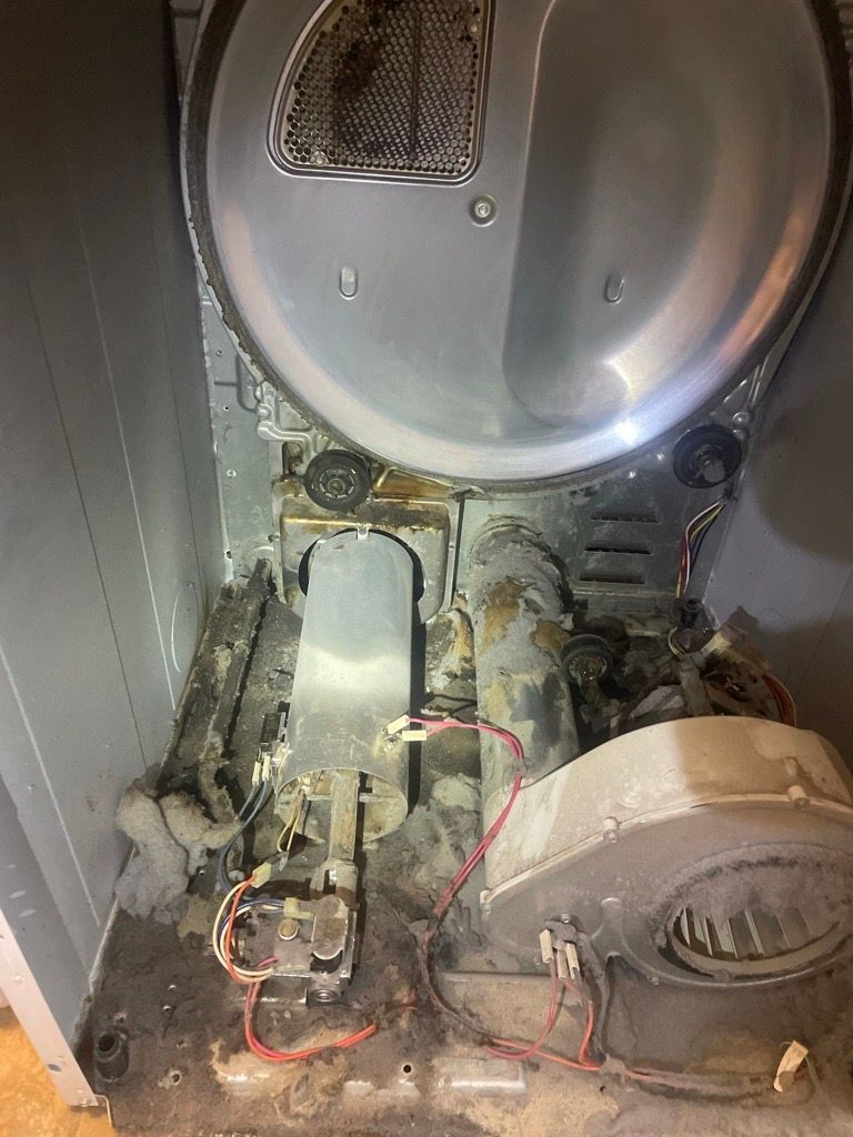 Interior of a dryer with the top open, showing the drum, heating element, and exhaust ducting, all coated in lint.