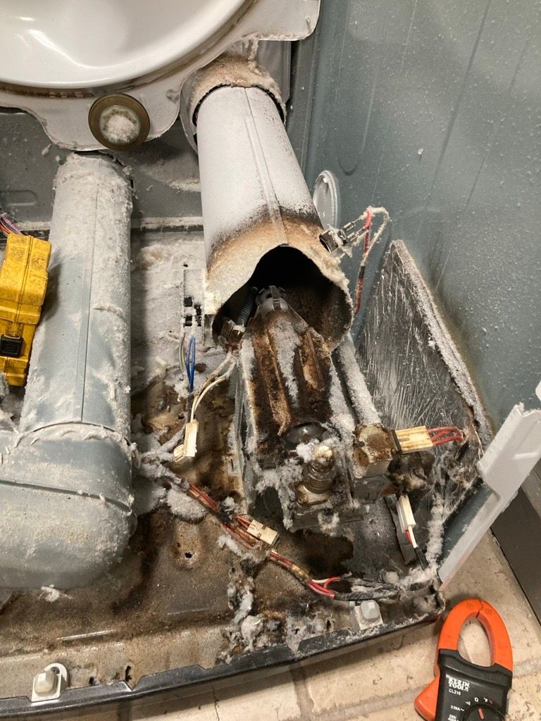 Damaged dryer interior with charred components and debris. Wires and vents are visible.