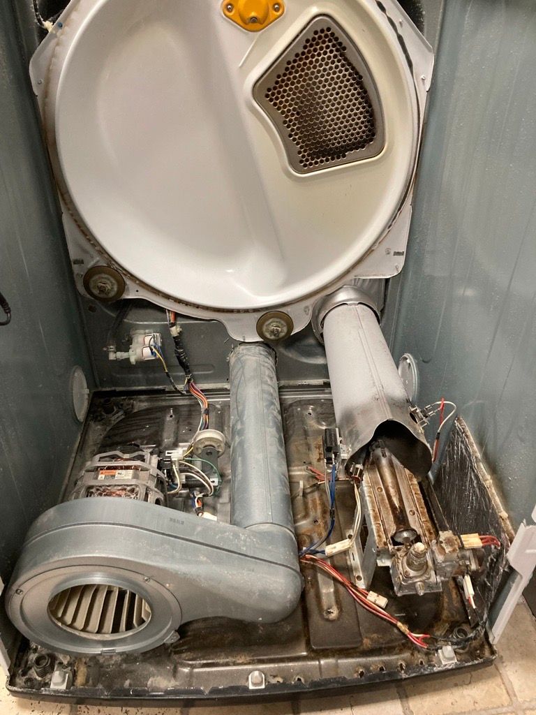 Interior of a dryer with the top and back panels removed, showing the drum, motor, heating element, and lint filter.