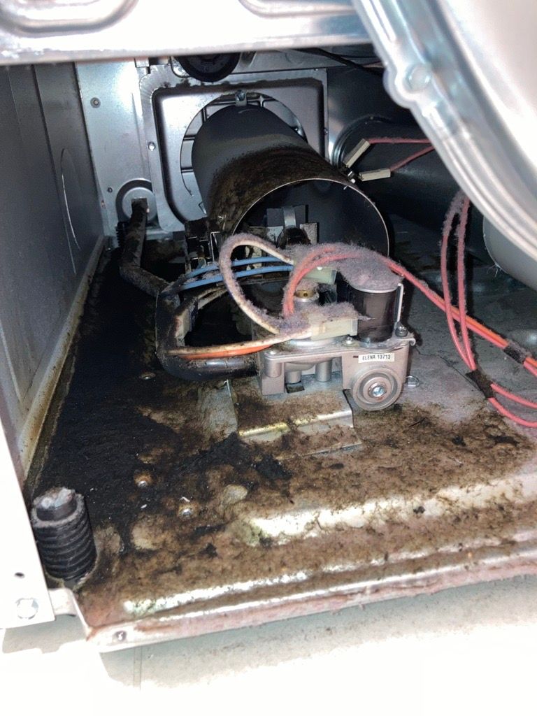 Inside of a gas dryer showing a dirty compartment, gas valve, and exhaust tube.