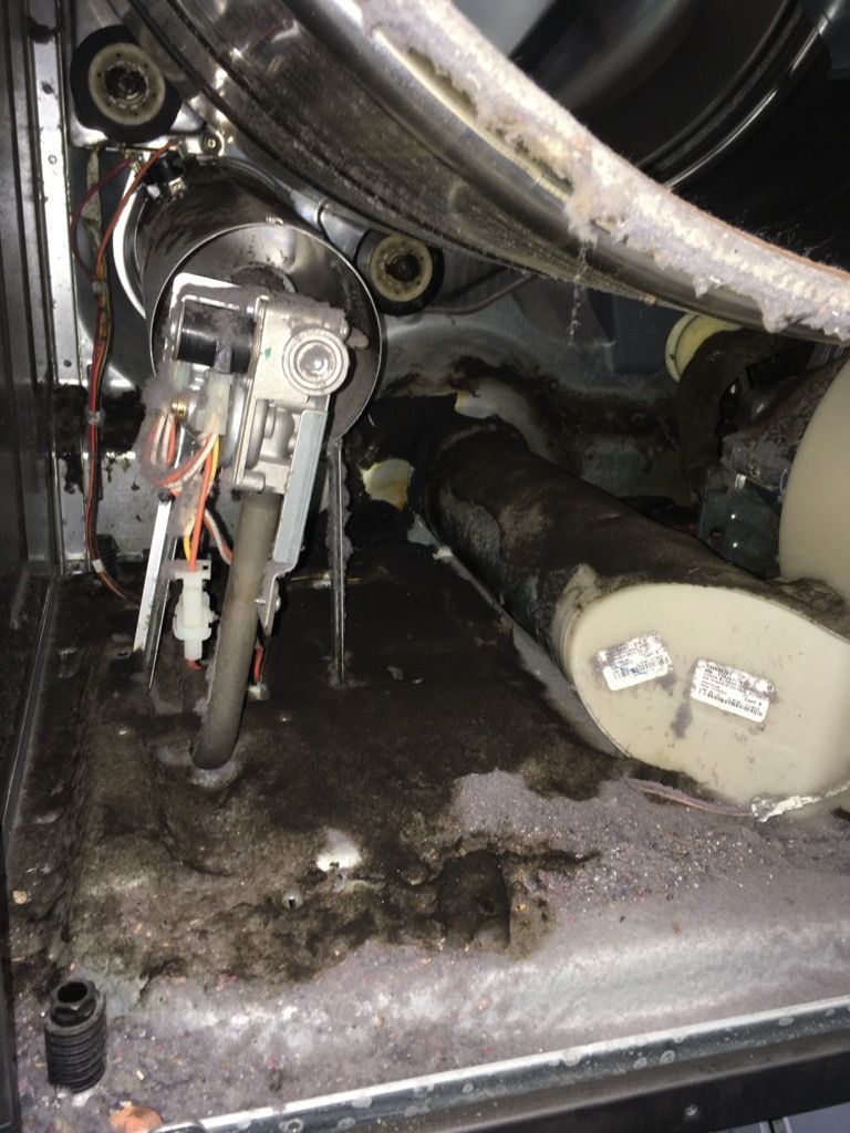 Interior of a dirty clothes dryer, showing a motor, drum, and lint accumulation.