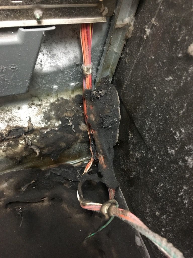 Burnt electrical wiring, black char, inside a vehicle compartment.