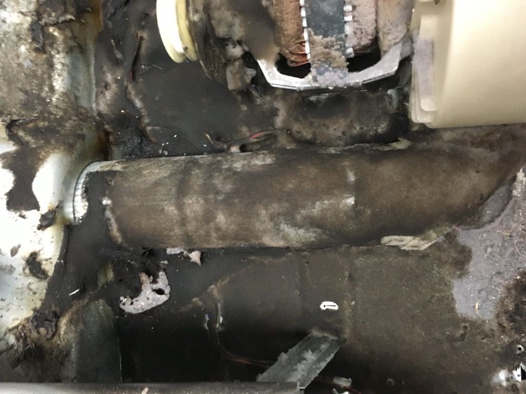 Interior view of a damaged appliance. Dark, charred residue covers components and surrounding surfaces.