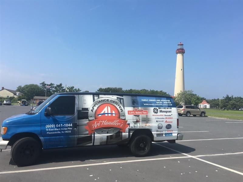 Blue service van with logo parked, lighthouse in background, sunny day.