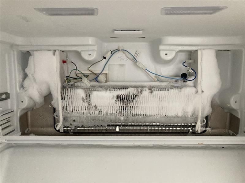 Interior of a refrigerator with a thick layer of ice covering the cooling components and surrounding walls.