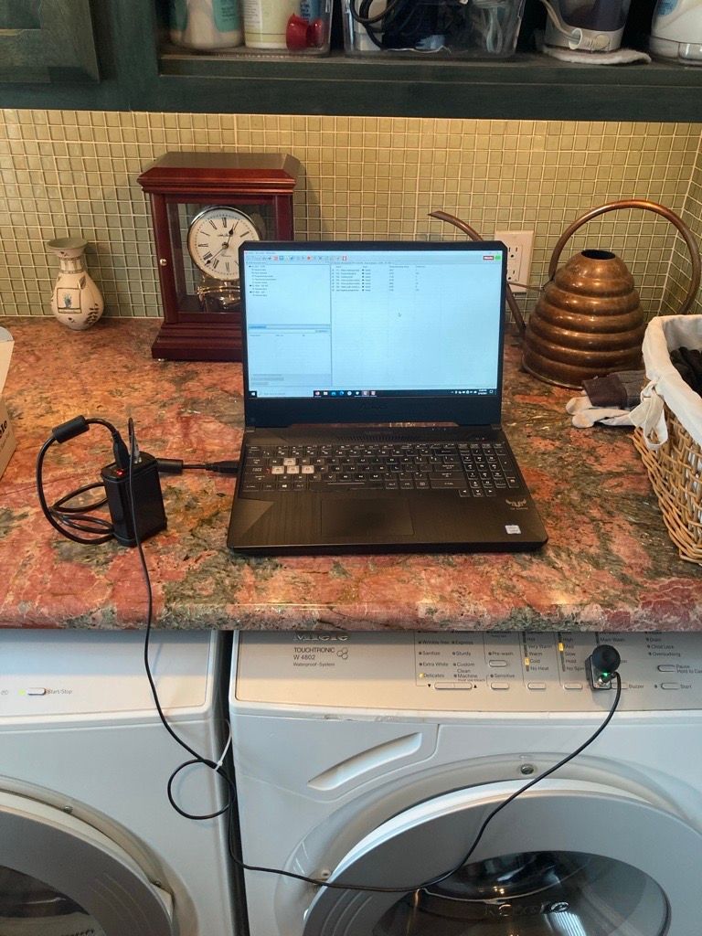 Laptop on a washing machine, connected to a sensor. A clock, vase, and decor are on the counter behind it.