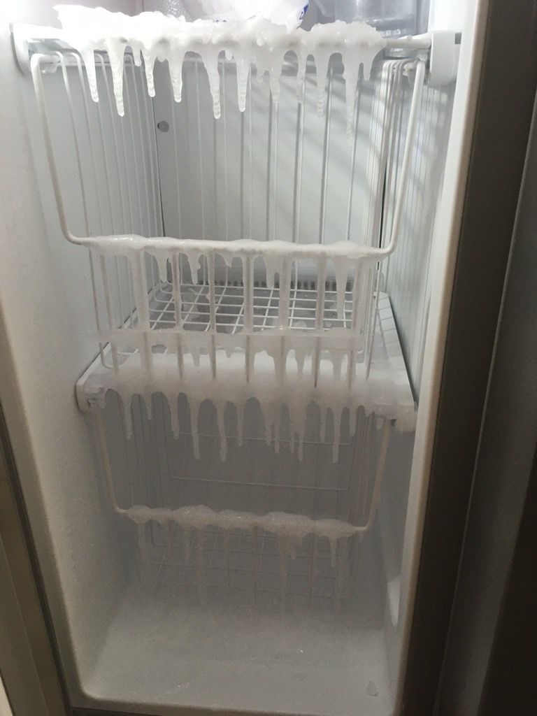 Freezer interior with heavy ice buildup on shelves and ceiling; an open door.