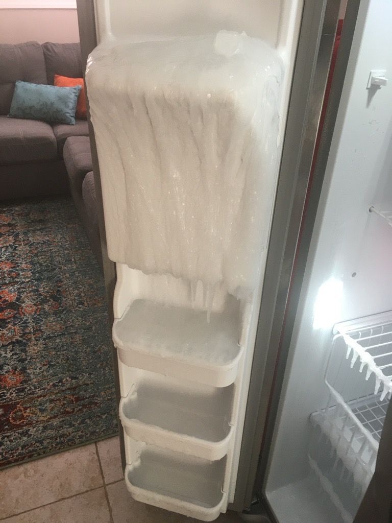 Refrigerator shelves encased in thick ice; door open, interior lit.