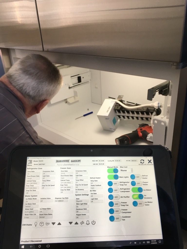 Person repairing a refrigerator, using a tablet with diagnostic software.