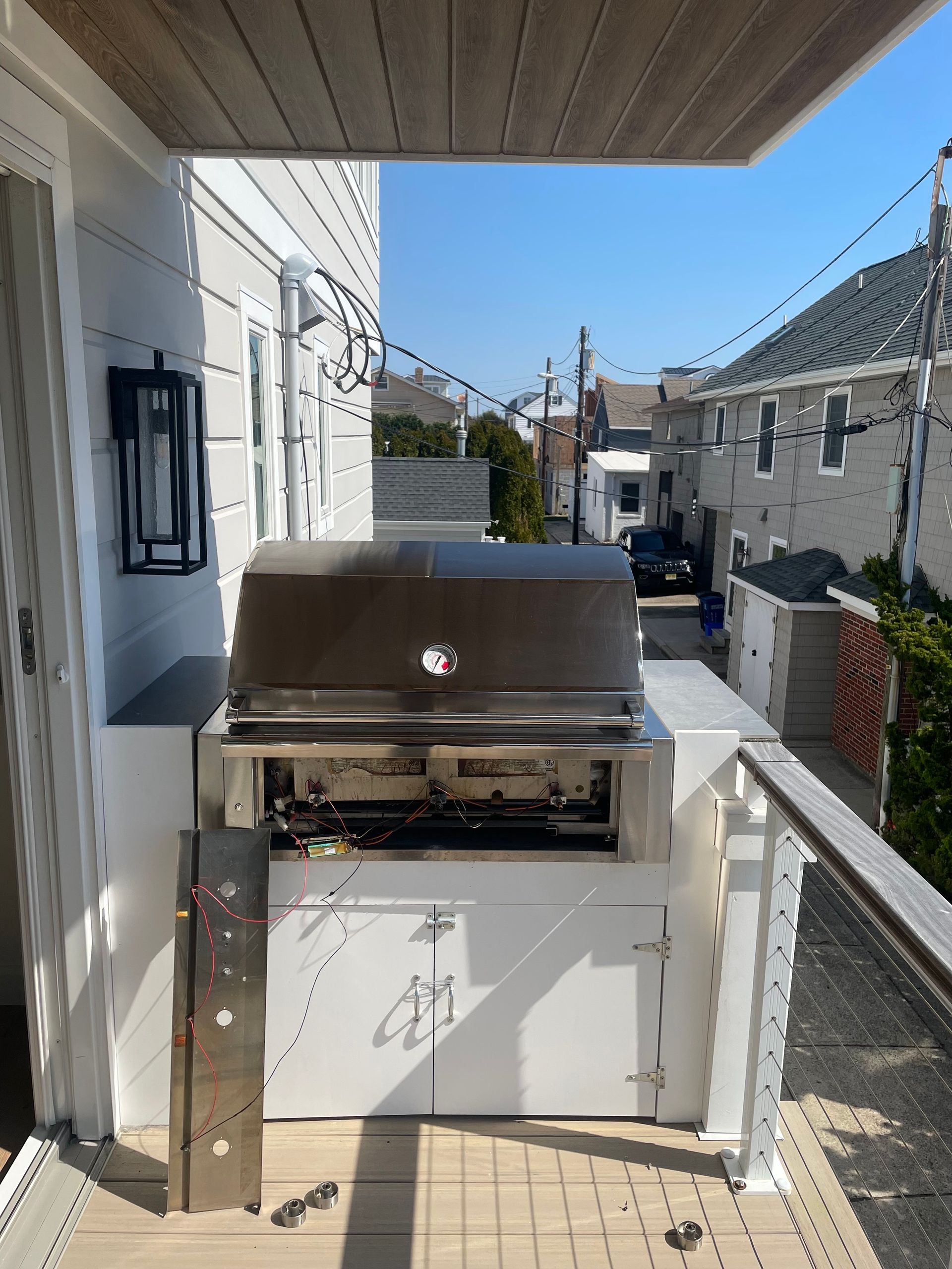 Outdoor grill built into white cabinets on a deck, with a view of a street.