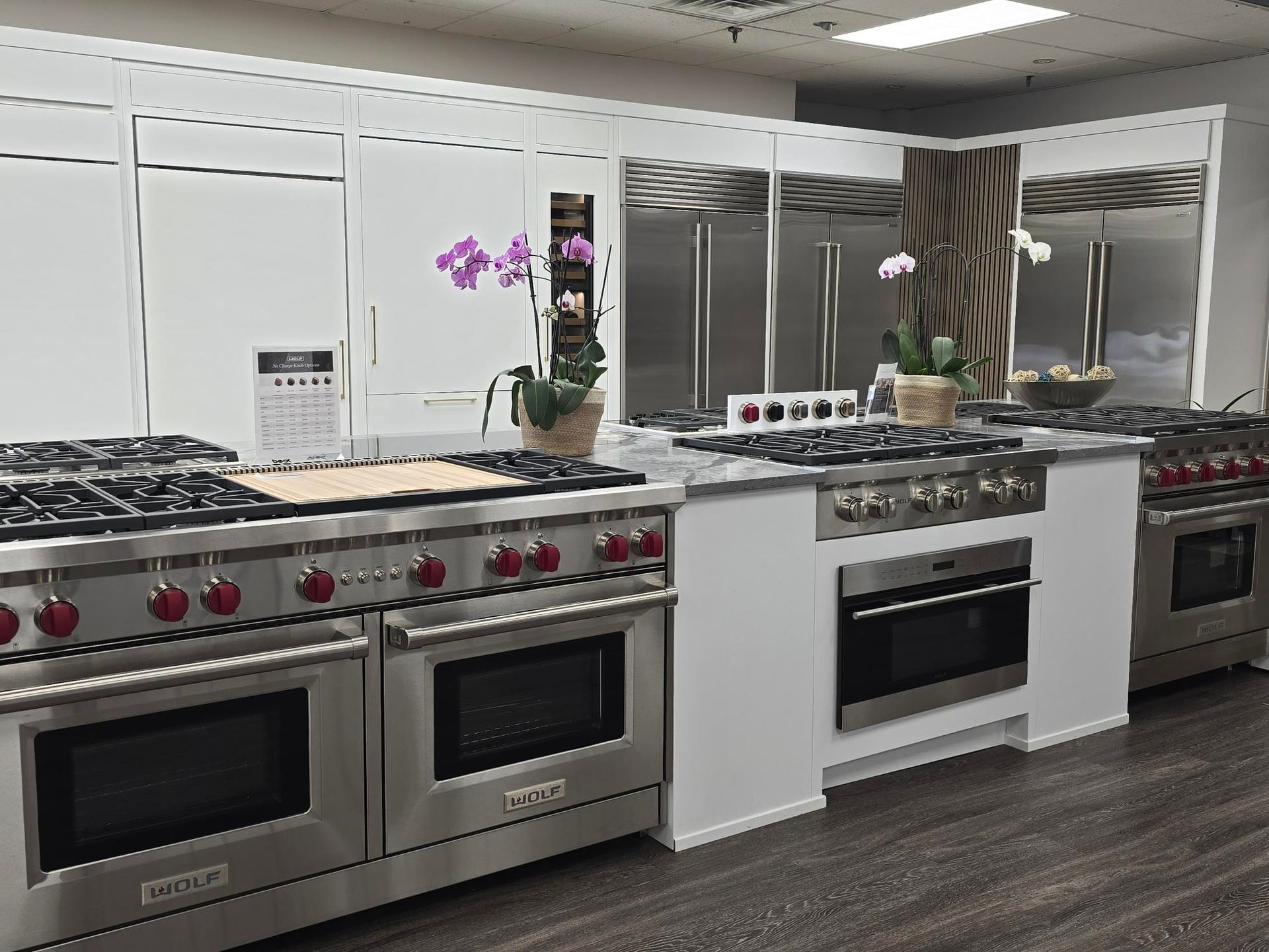 Kitchen appliances on display, stainless steel ranges with ovens, white cabinets, and orchids.