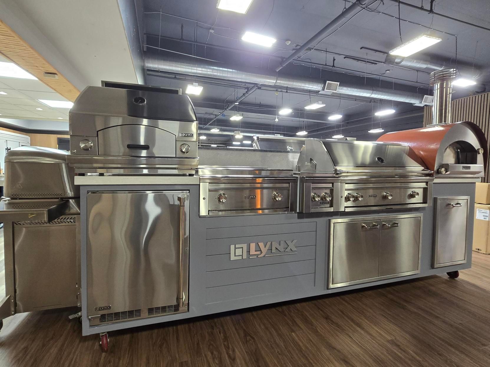 Outdoor kitchen with stainless steel grills, doors, and a pizza oven on a gray base.
