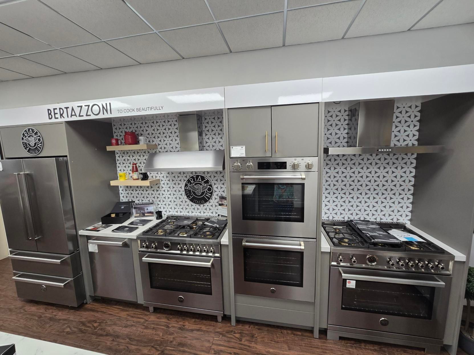A kitchen appliance showroom featuring Bertazzoni appliances. Stainless steel refrigerators, ovens, and cooktops on display.