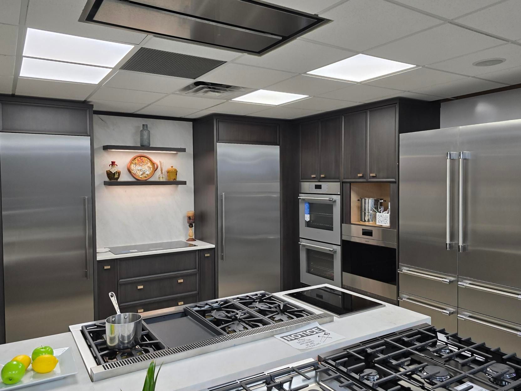 Modern kitchen with stainless steel appliances, dark cabinetry, and a large central cooktop island.