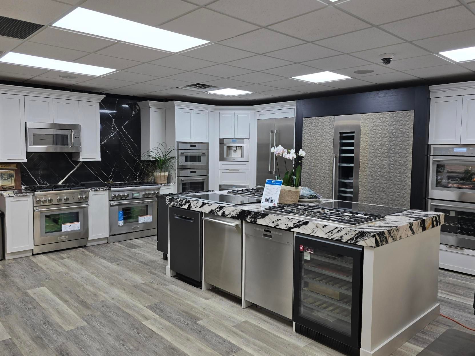 Kitchen showroom with stainless steel appliances, white cabinets, and granite countertops.